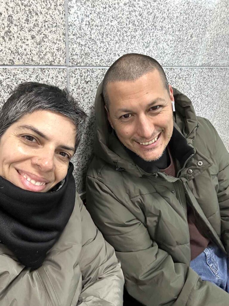 Imagem mostra o casal aguardando o trem na sala de espera da estação.